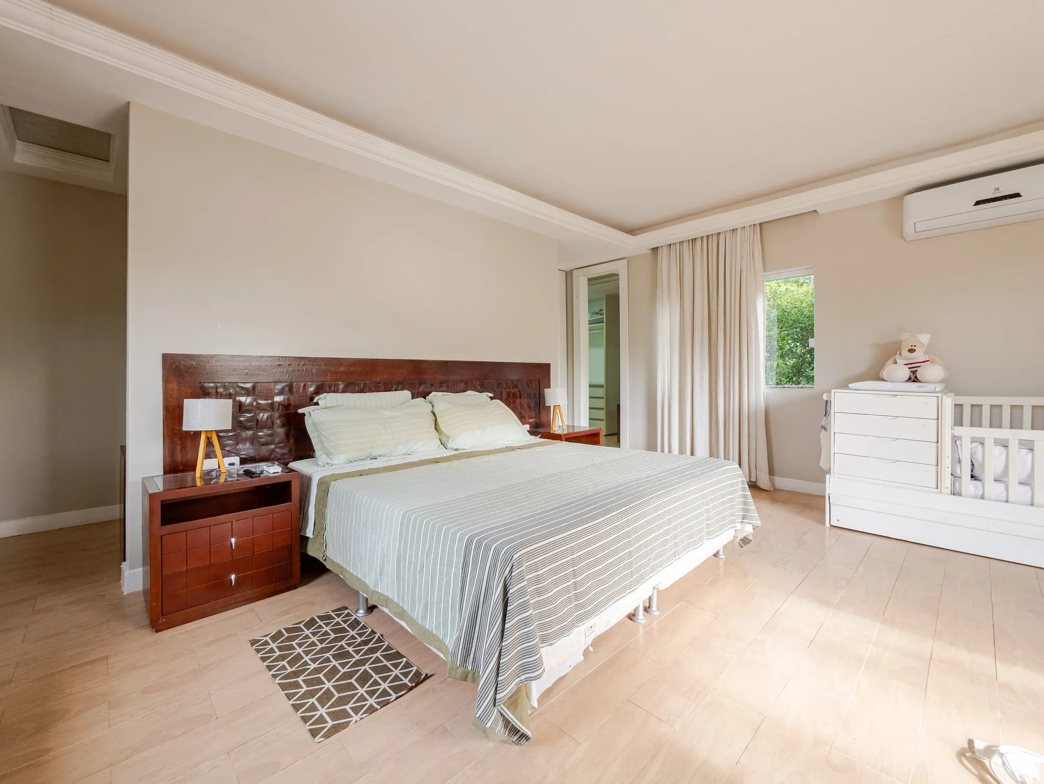 Suíte master com cabeceira de madeira, cama king e berço branco