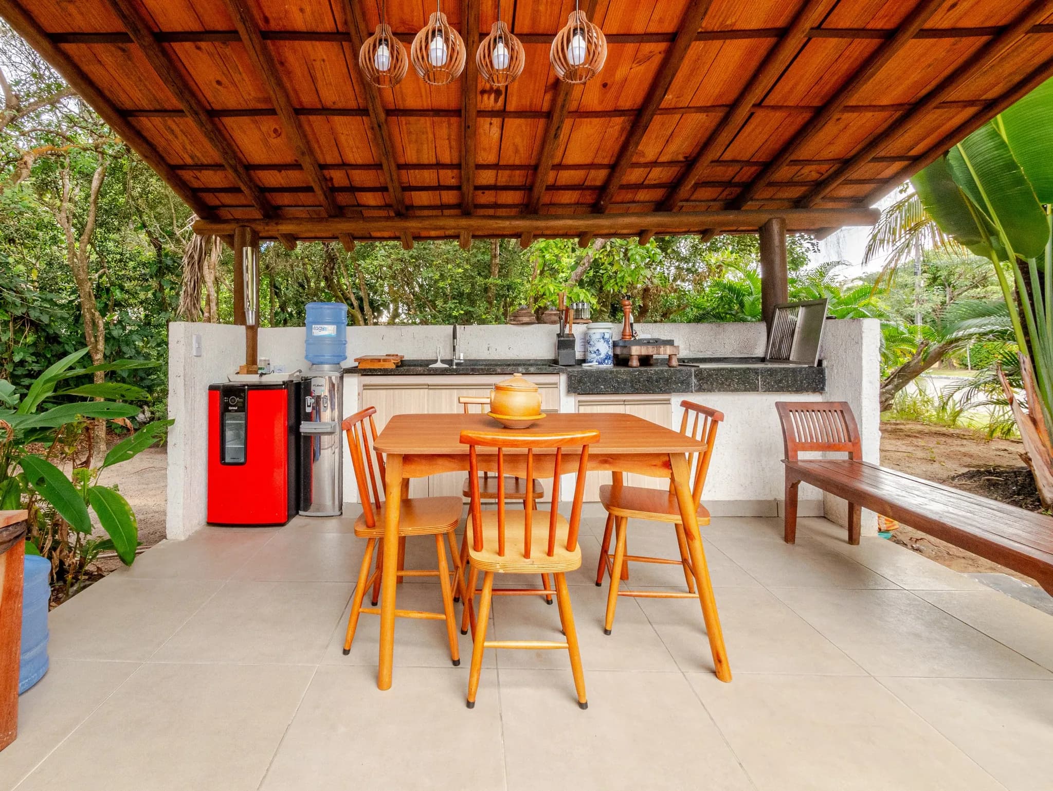 Área gourmet externa com mesa e cadeiras de madeira, bancada e telhado de madeira