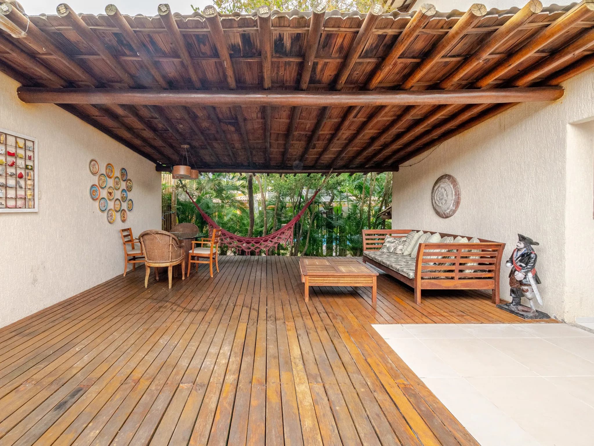 Varanda ampla de deck de madeira com rede, sofá e mesa de apoio