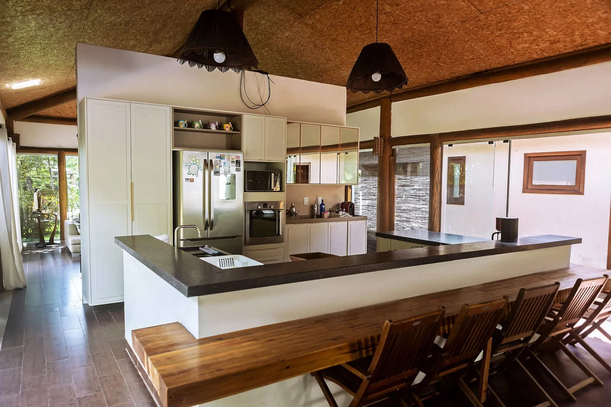 Visão geral da cozinha com ilha e banco de madeira sob luminárias de palha