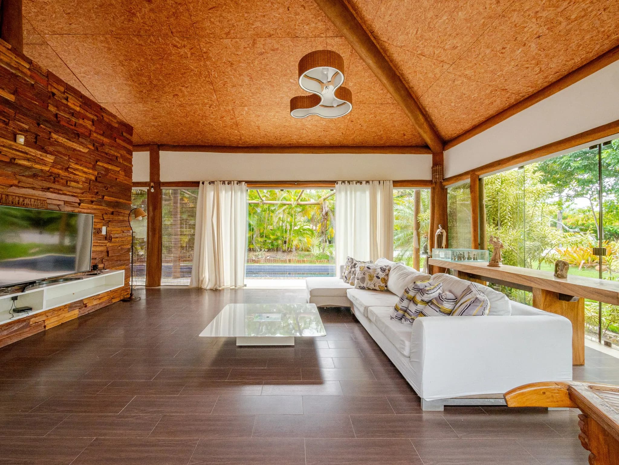 Sala com forro de madeira, parede revestida de madeira e sofá branco diante das janelas de vidro