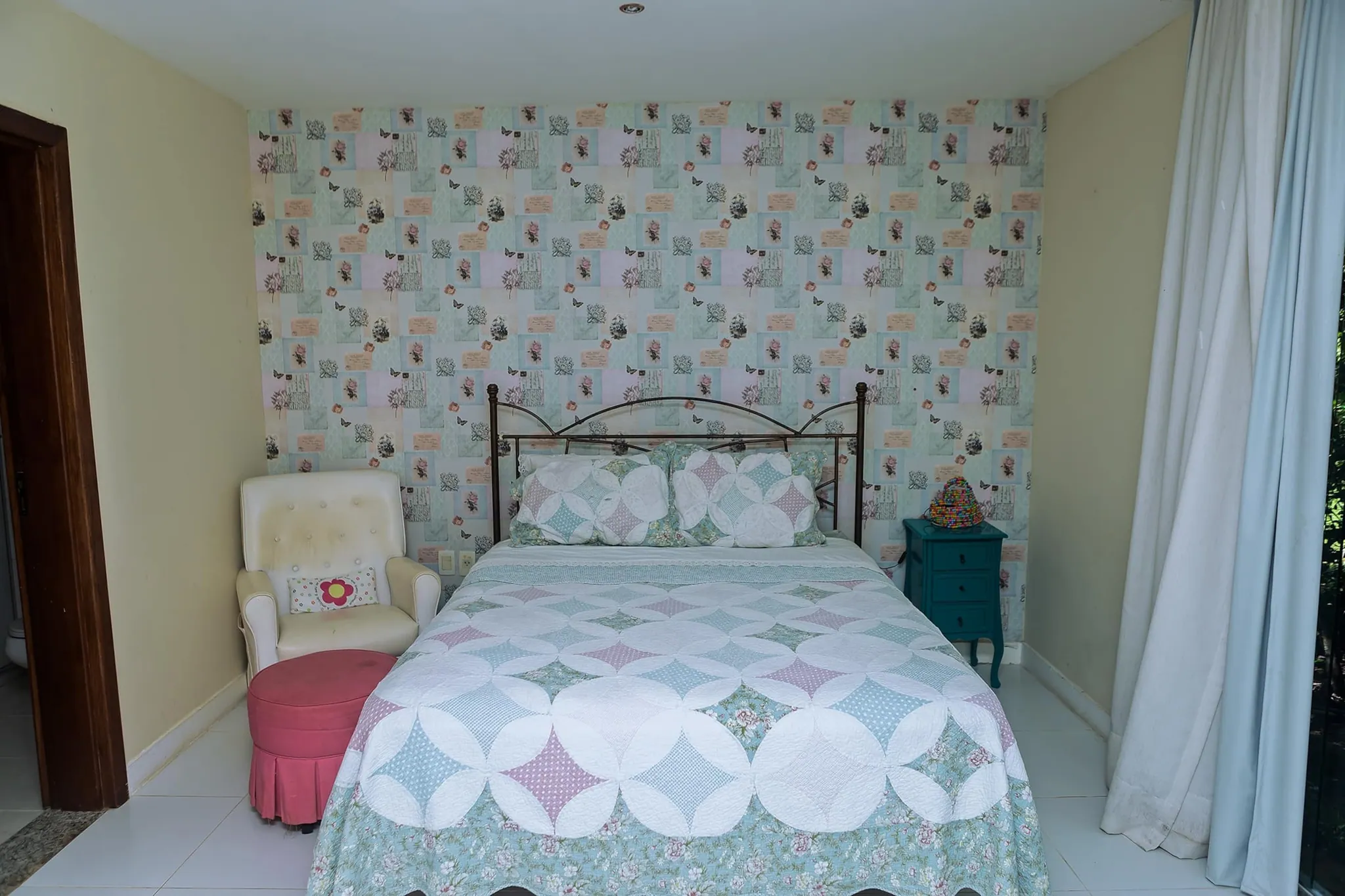 Suíte com cama de casal, cabeceira de ferro e parede com papel estampado