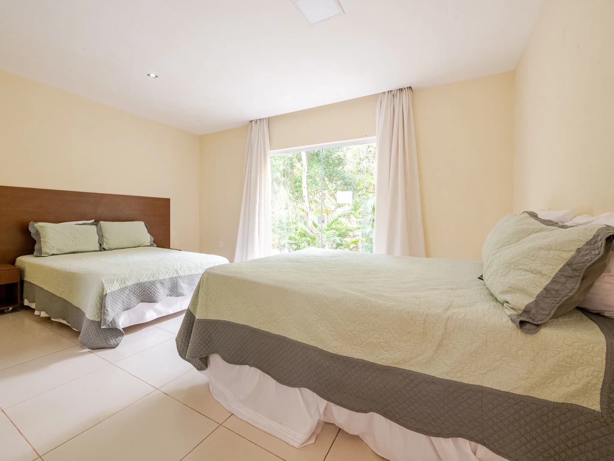 Suíte com cama de casal e cama de solteiro, roupa de cama em tons de verde