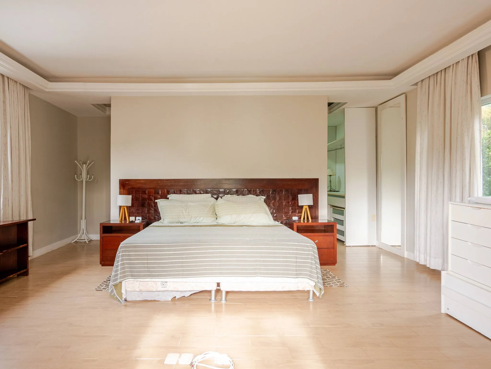 Suíte master com cama king, cortinas claras e piso de madeira clara